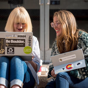 two girls working on laptops outside